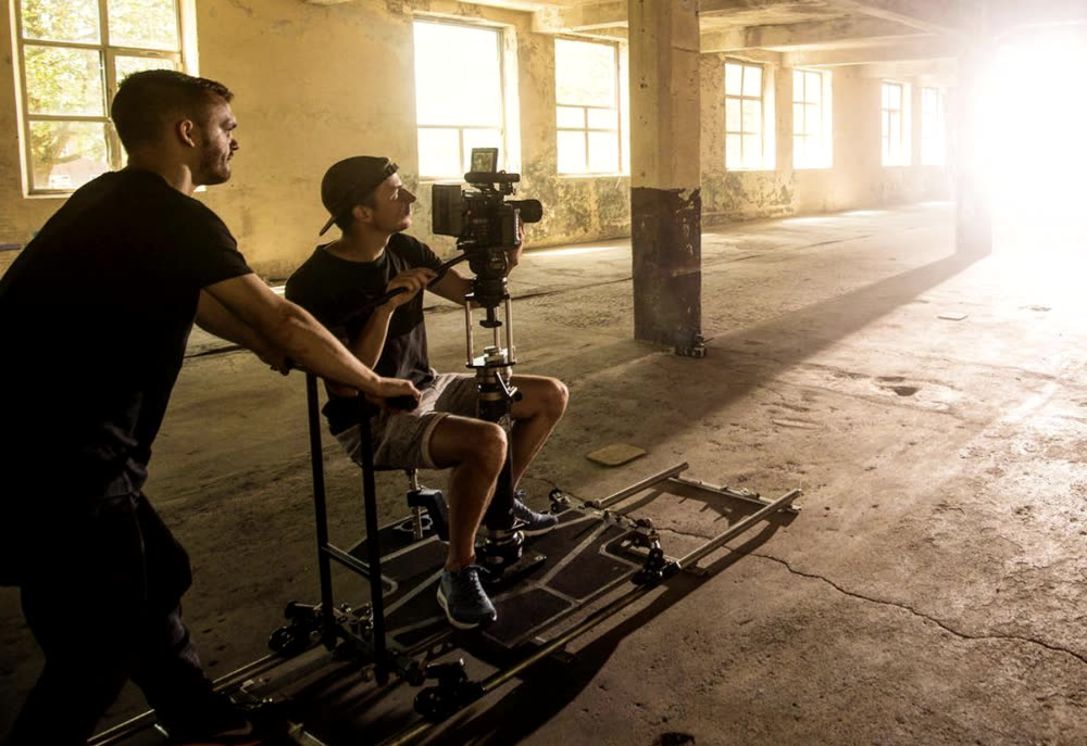 Two crew operating a camera dolly on rails in a warehouse